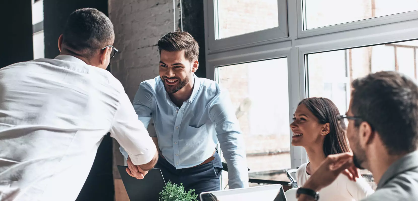 Young modern men in smart casual wear shaking hands and smiling while working in an office