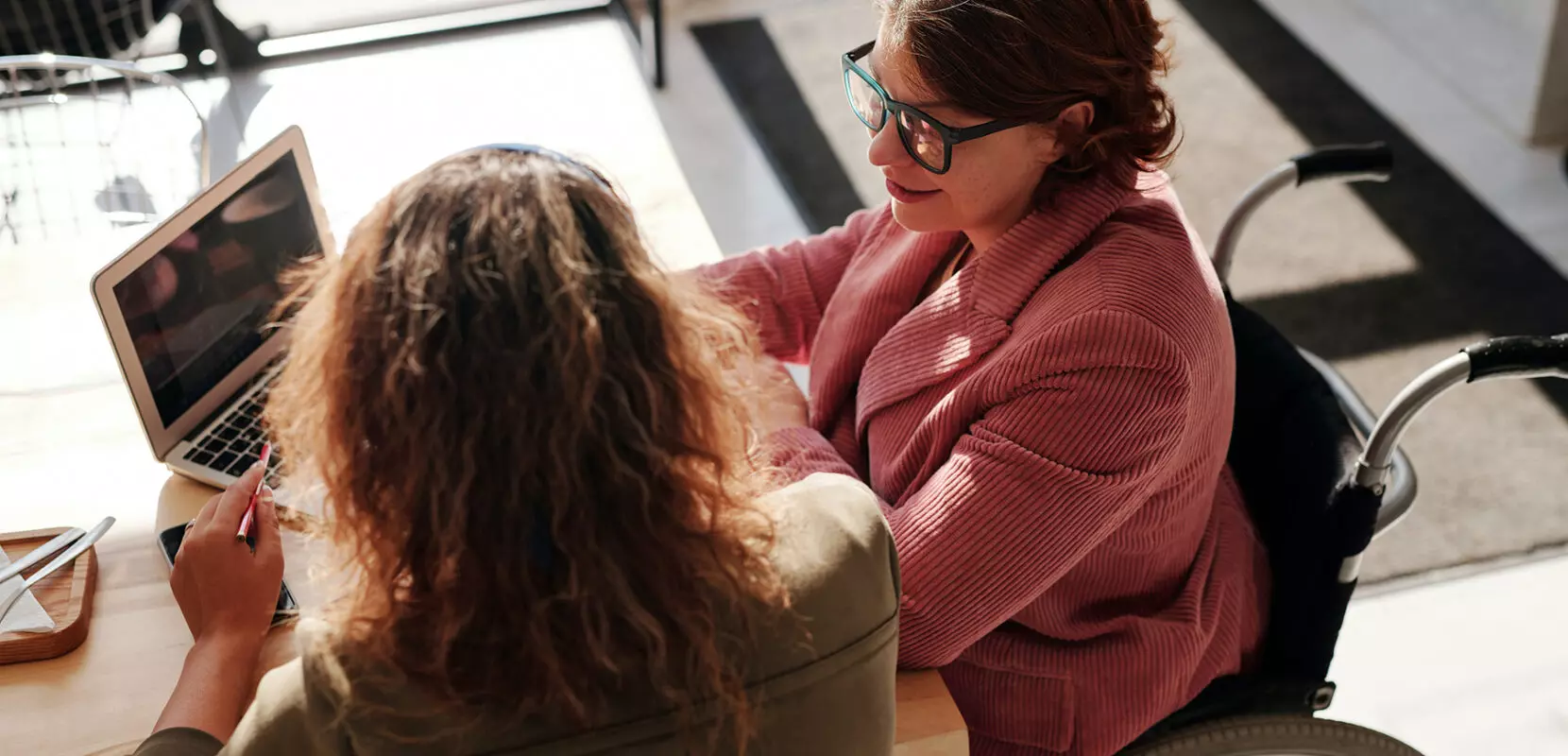 a woman in a wheelchair and another woman look at a computer and discuss year-end planning