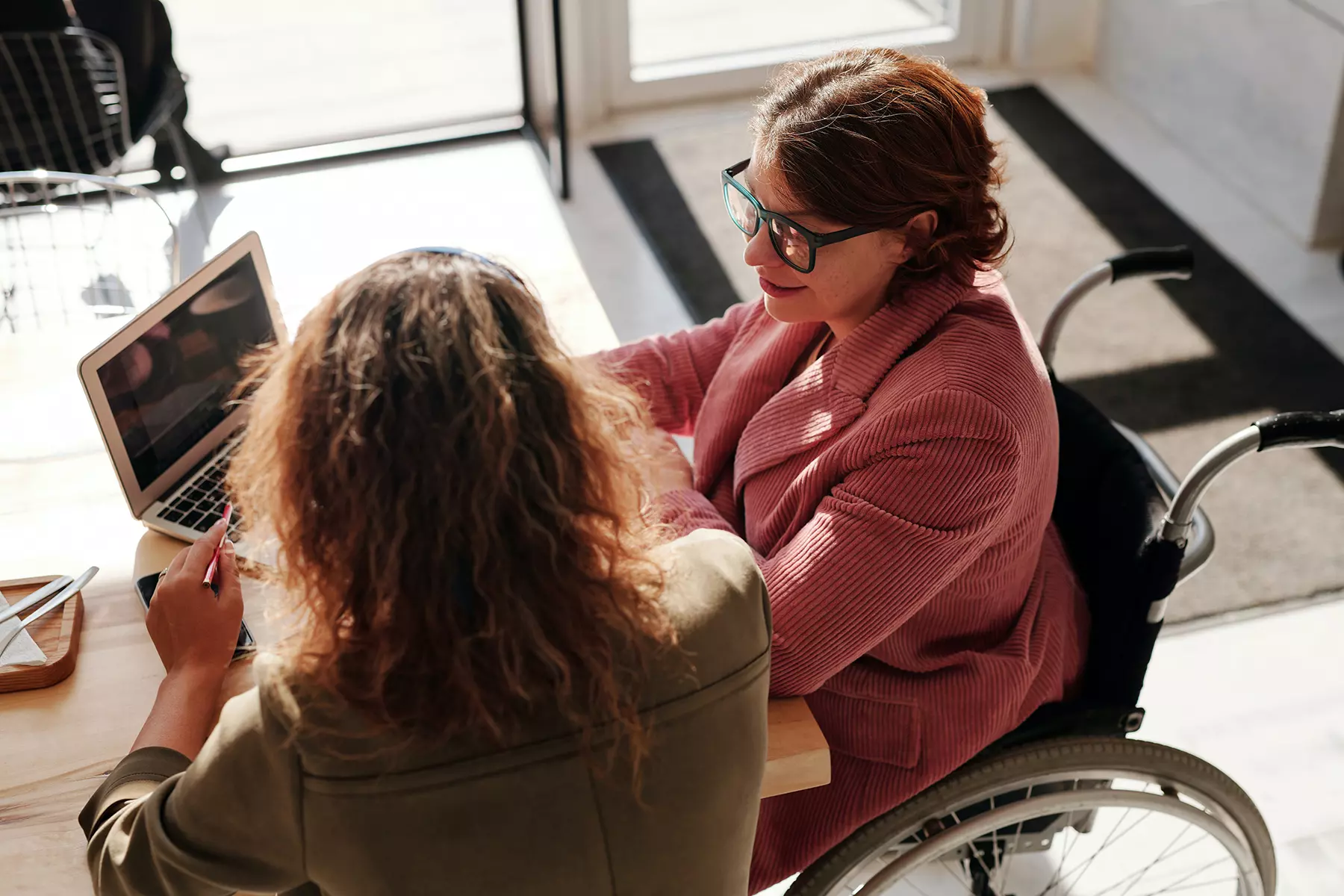 a woman in a wheelchair and another woman look at a computer and discuss year-end planning