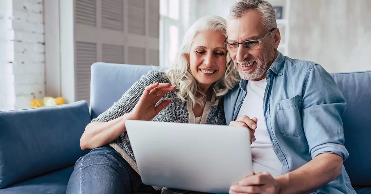 a couple on their computer smiling as they looking through their investments