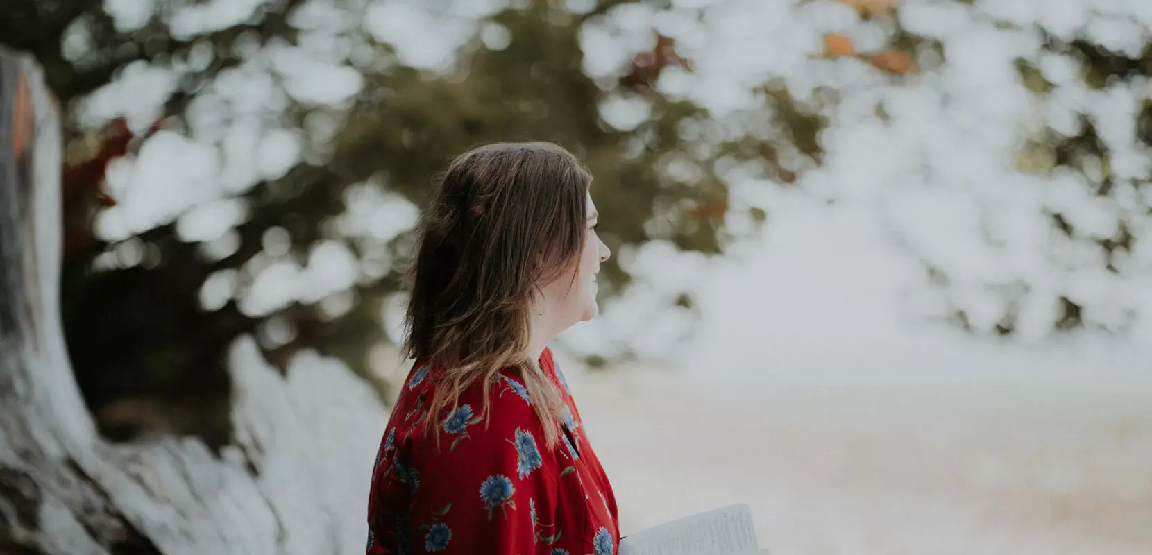 a woman stands outside by a waterfall reading her bible