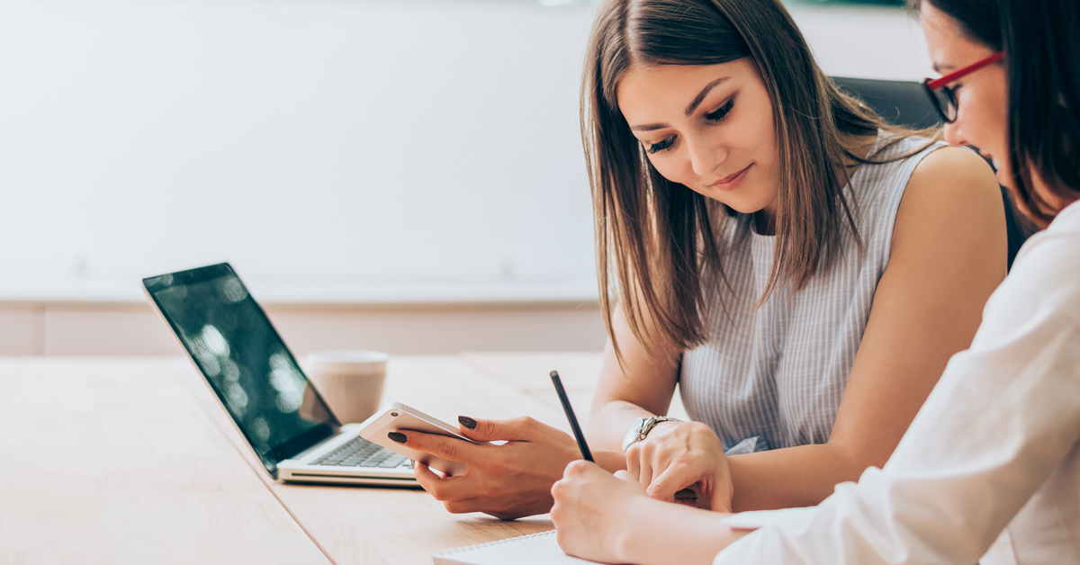 two women sit at a table looking over a spreadsheet