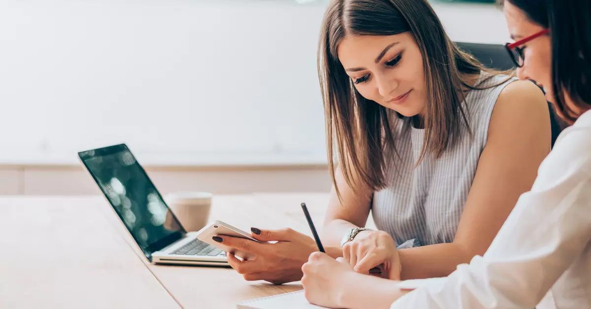 two women sit at a table looking over a spreadsheet
