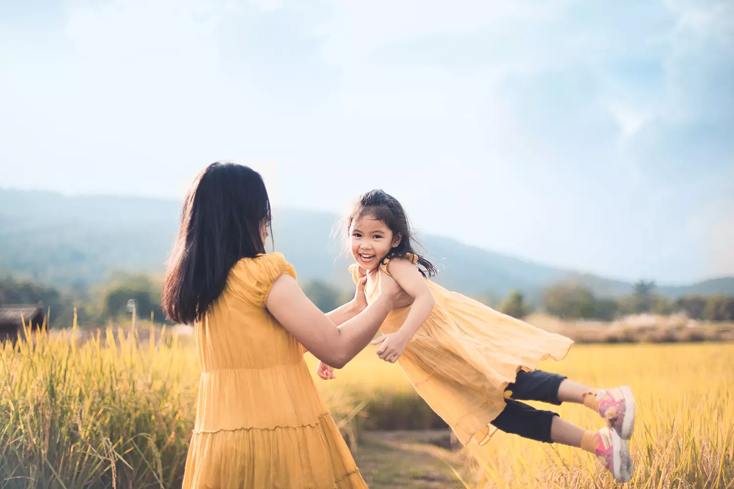 a mother spins her daughter around in a meadow