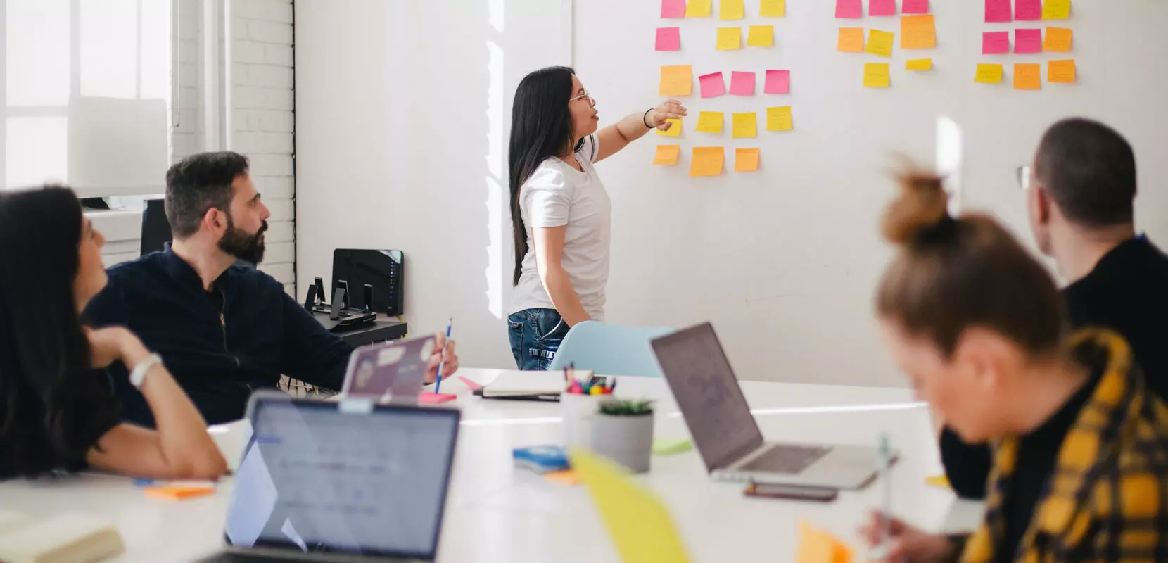 a meeting of a nonprofit around a table with a white board and sticky notes discussing fundraising ideas