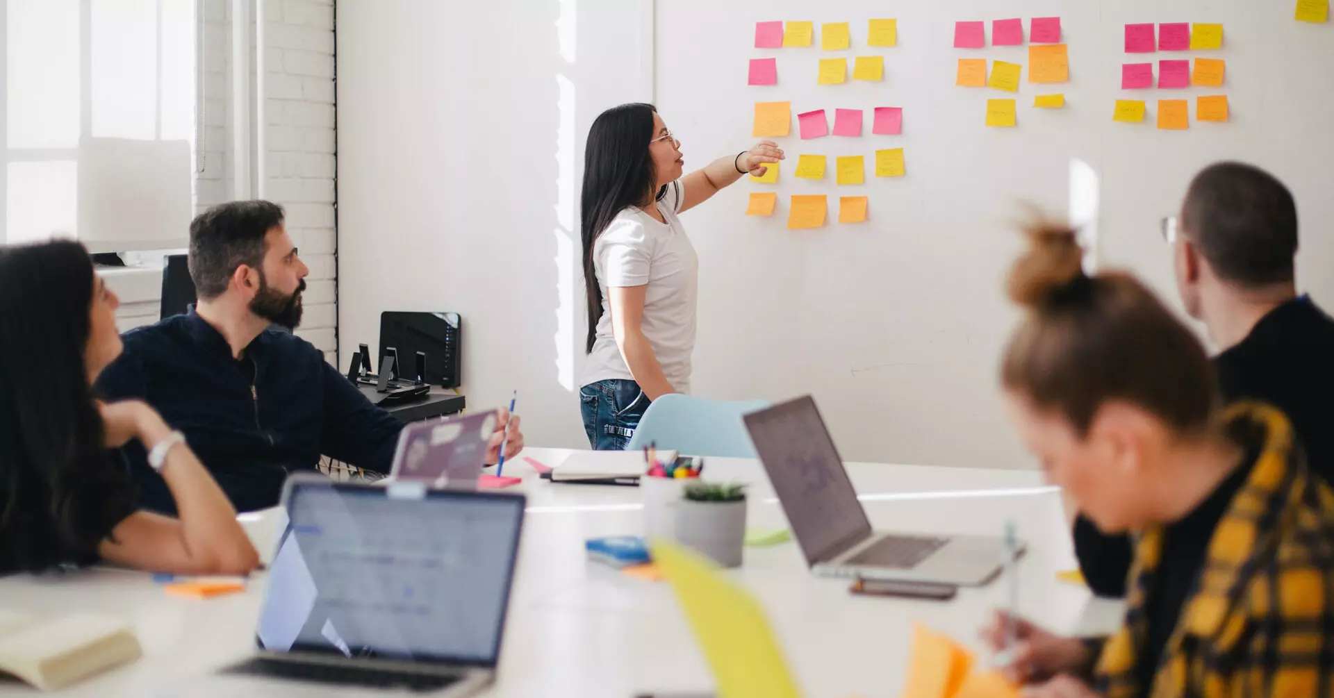 a meeting of a nonprofit around a table with a white board and sticky notes discussing fundraising ideas