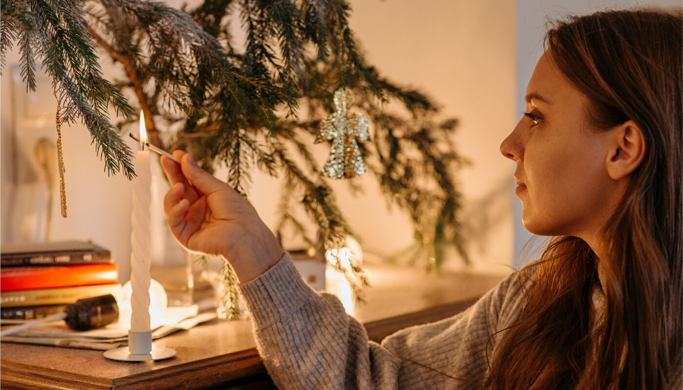 a woman lights a candle by the christmas tree sharing the december spirit