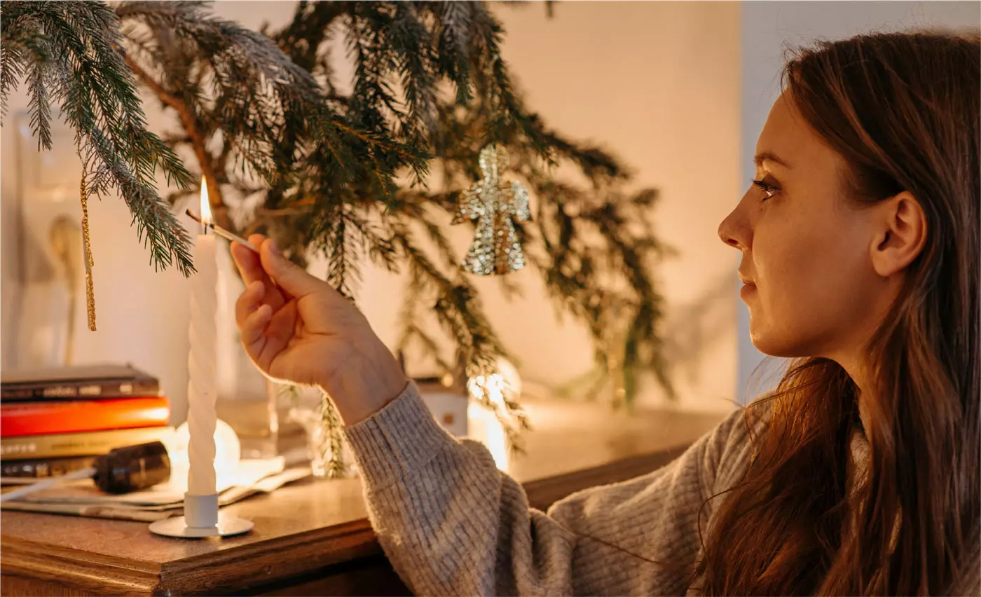 a woman lights a candle by the christmas tree sharing the december spirit