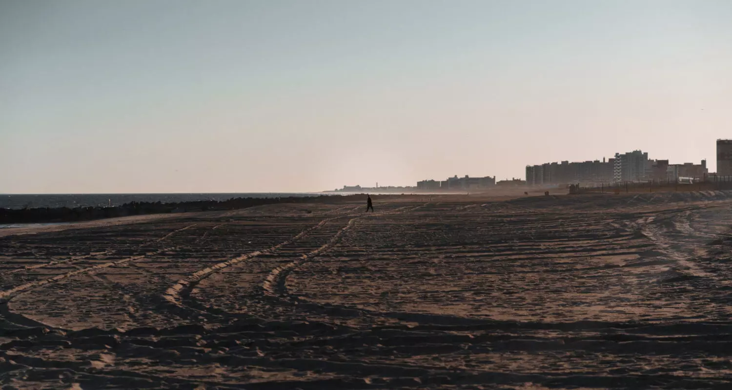 one man walks through aa desert with a city in the background
