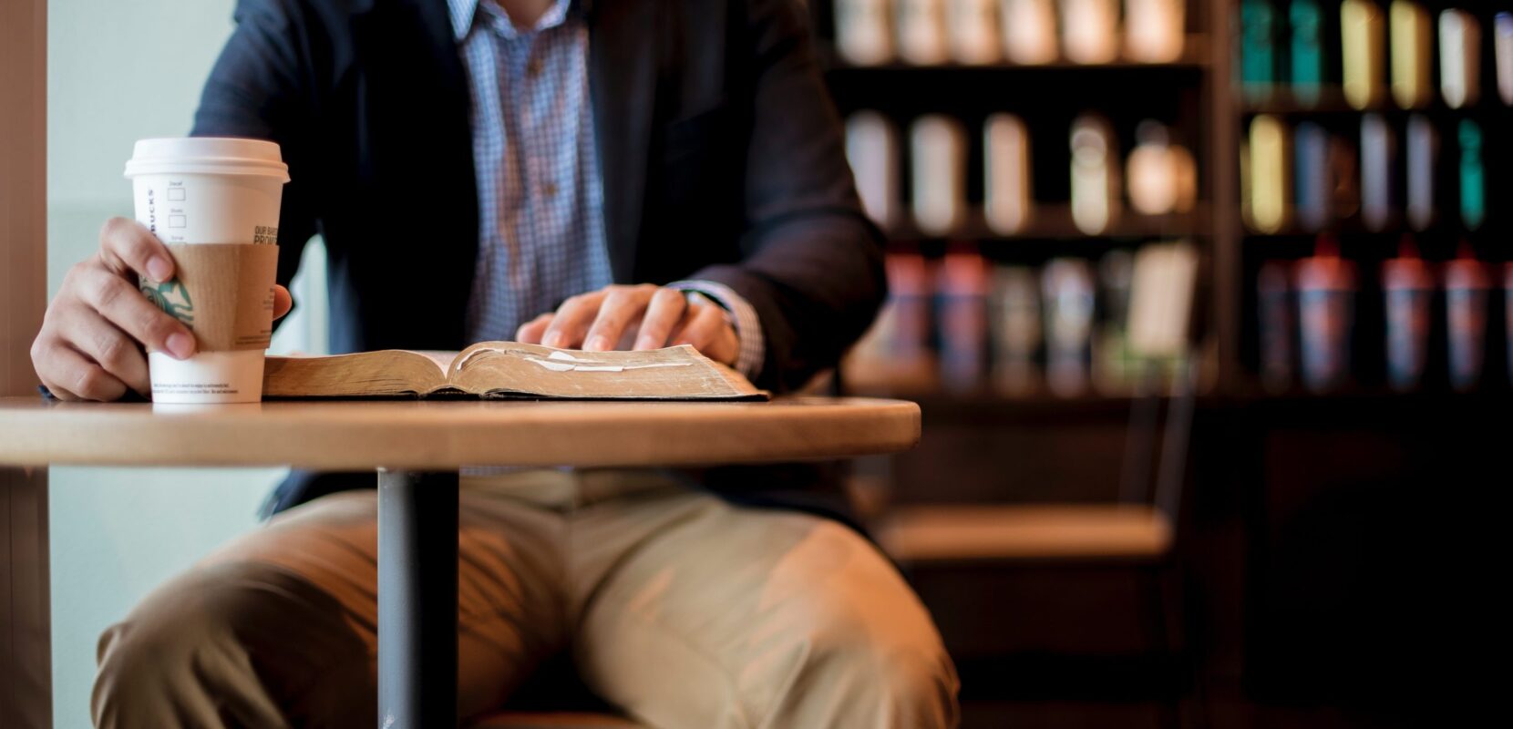 a man sits at a coffee shop with a coffee and his bible open