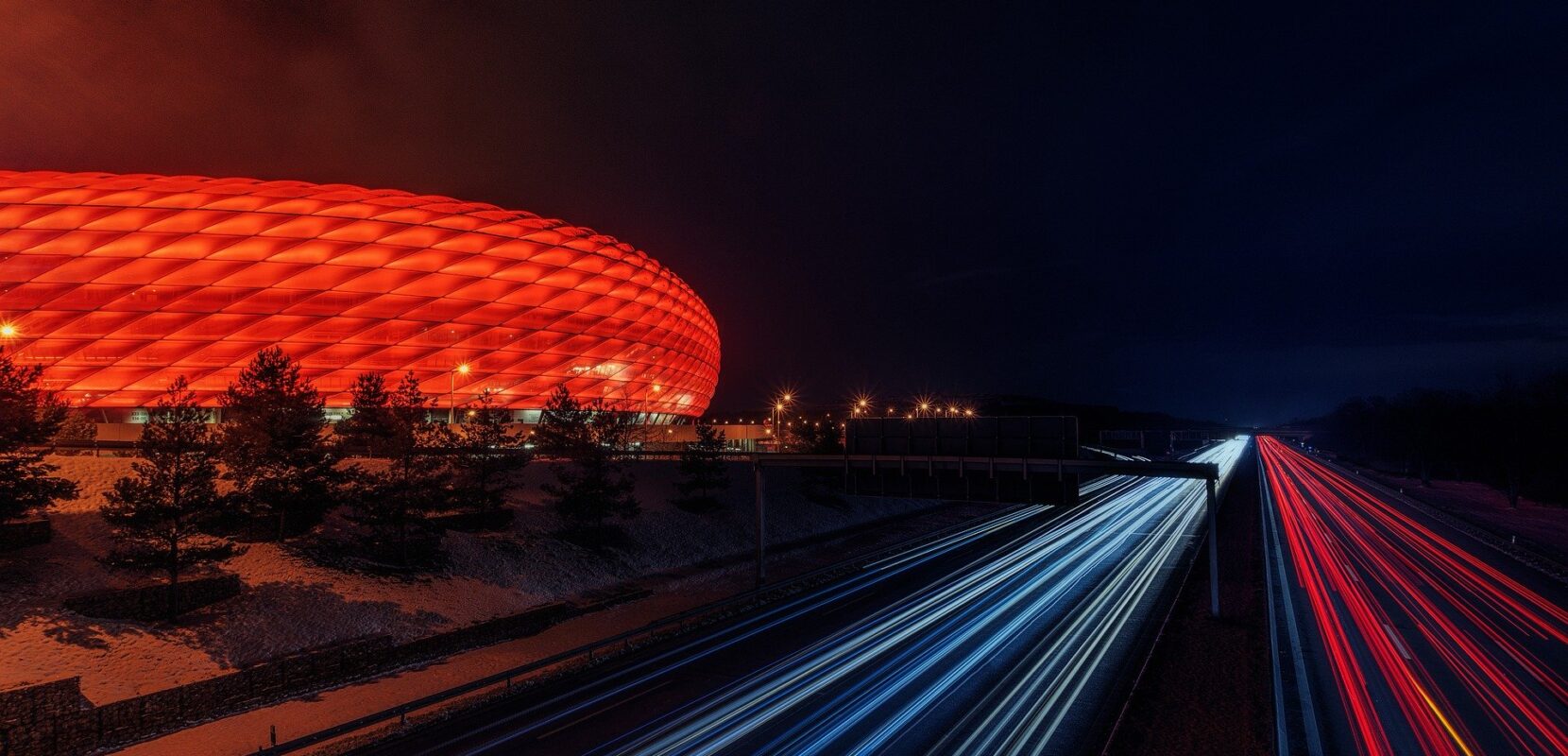 a football stadium is lit up with read lights beside a highway with streams of blue and red lights