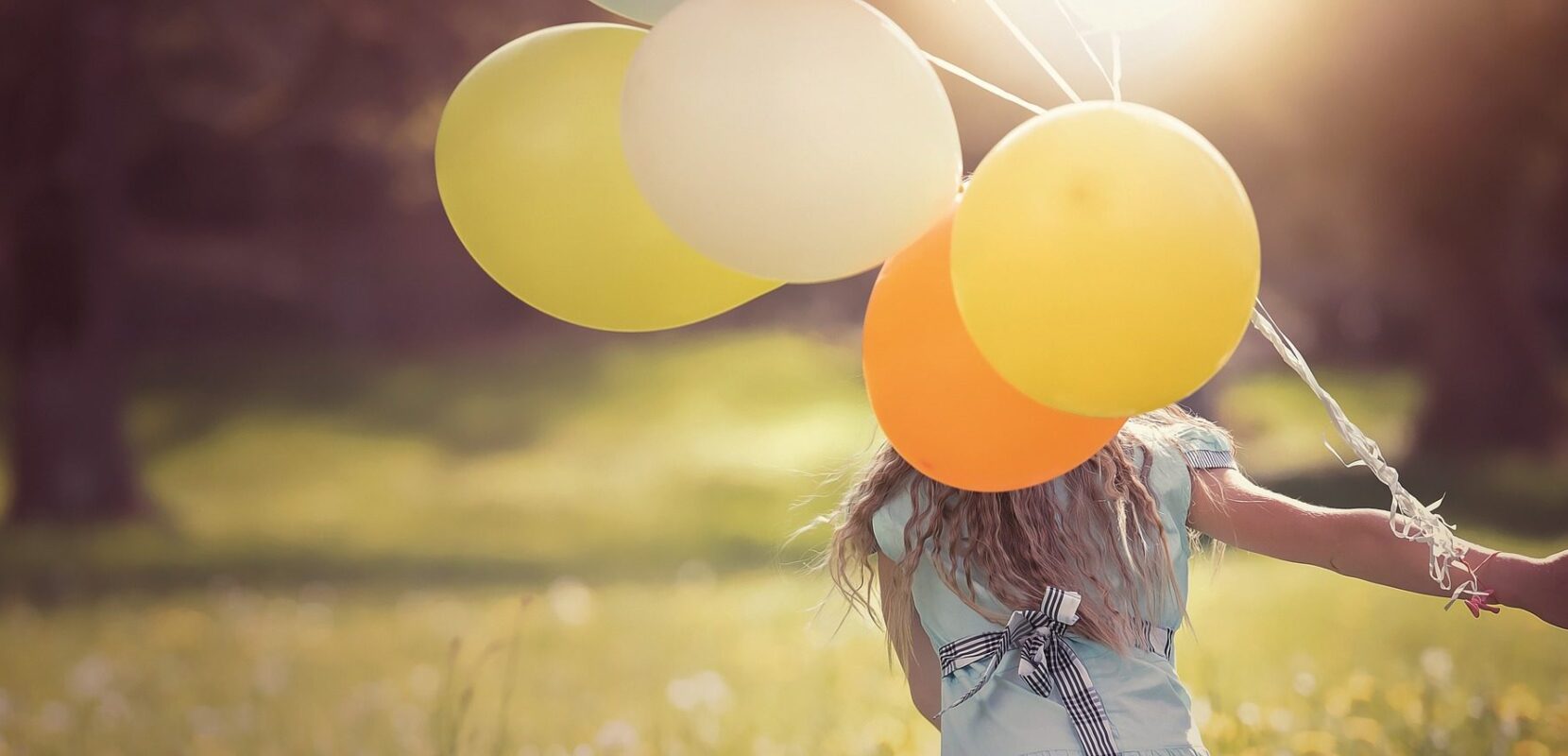 a little girl running through a meadow carrying balloons
