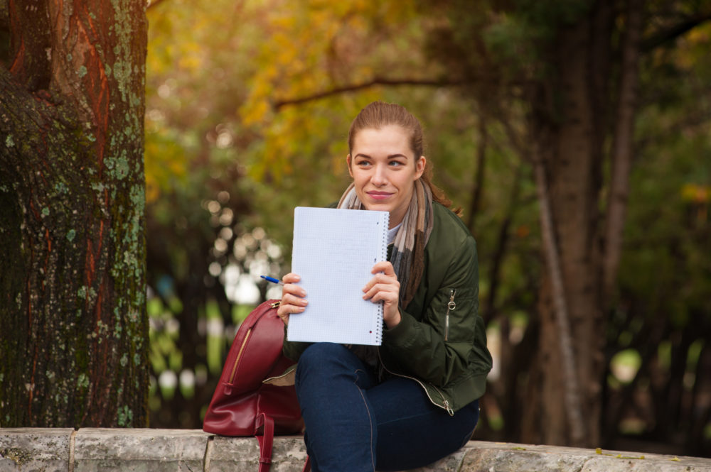 a young woman sits on a bench in the park with a notebook