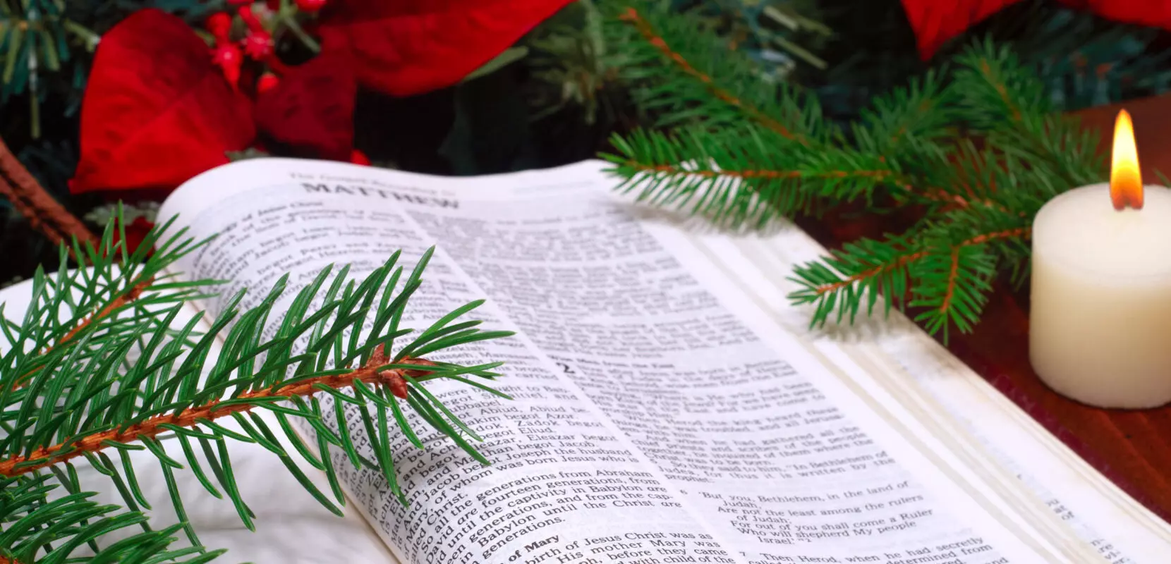the bible open to the book of matthew next to a lit candle and garland