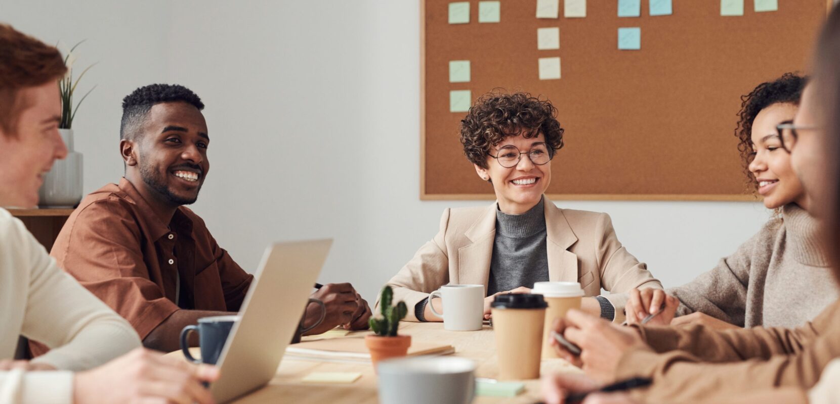 a group of coworkers sit at a table with coffee and computers discussing development culture