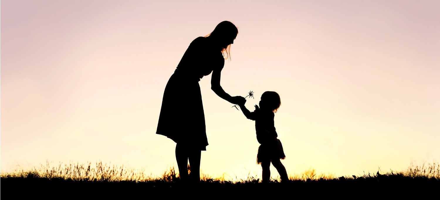a mother hands her daughter a flower at sunset