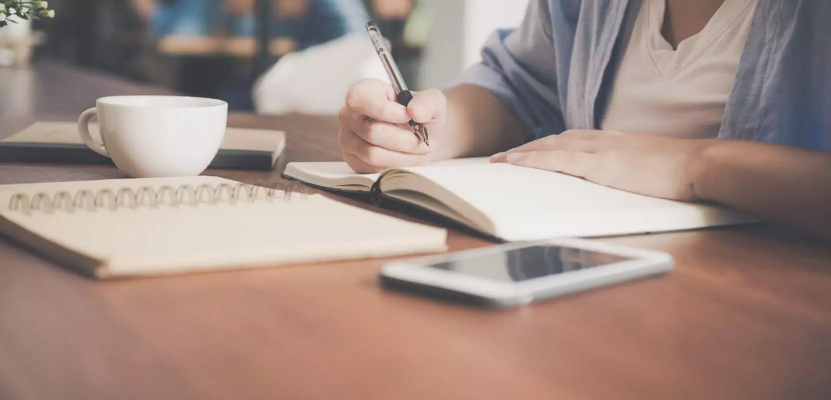 woman writing a message in a notebook at a coffee shop